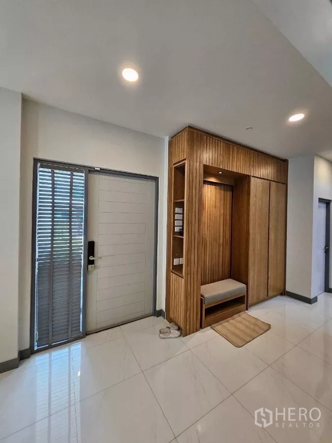 Detached House for rent or sale in Bang Phli, Samut Prakan - Entry foyer with built‑in wooden shoe cabinet and bench, digital door lock, and glossy tiled floor.
