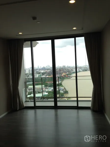 Condominium for rent in Bang Sue, Bangkok - Living area with floor-to-ceiling windows and balcony facing river and skyline.