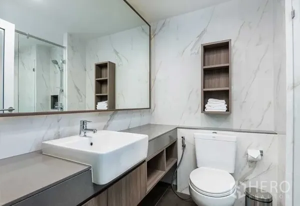 Apartment for rent in Huai Khwang, Bangkok - Contemporary bathroom with marble-effect walls, wide vanity, large mirror, and glass shower.