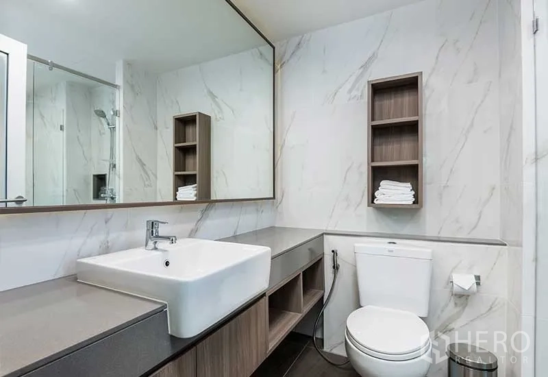 Apartment for rent in Huai Khwang, Bangkok - Contemporary bathroom with marble-effect walls, wide vanity, large mirror, and glass shower.
