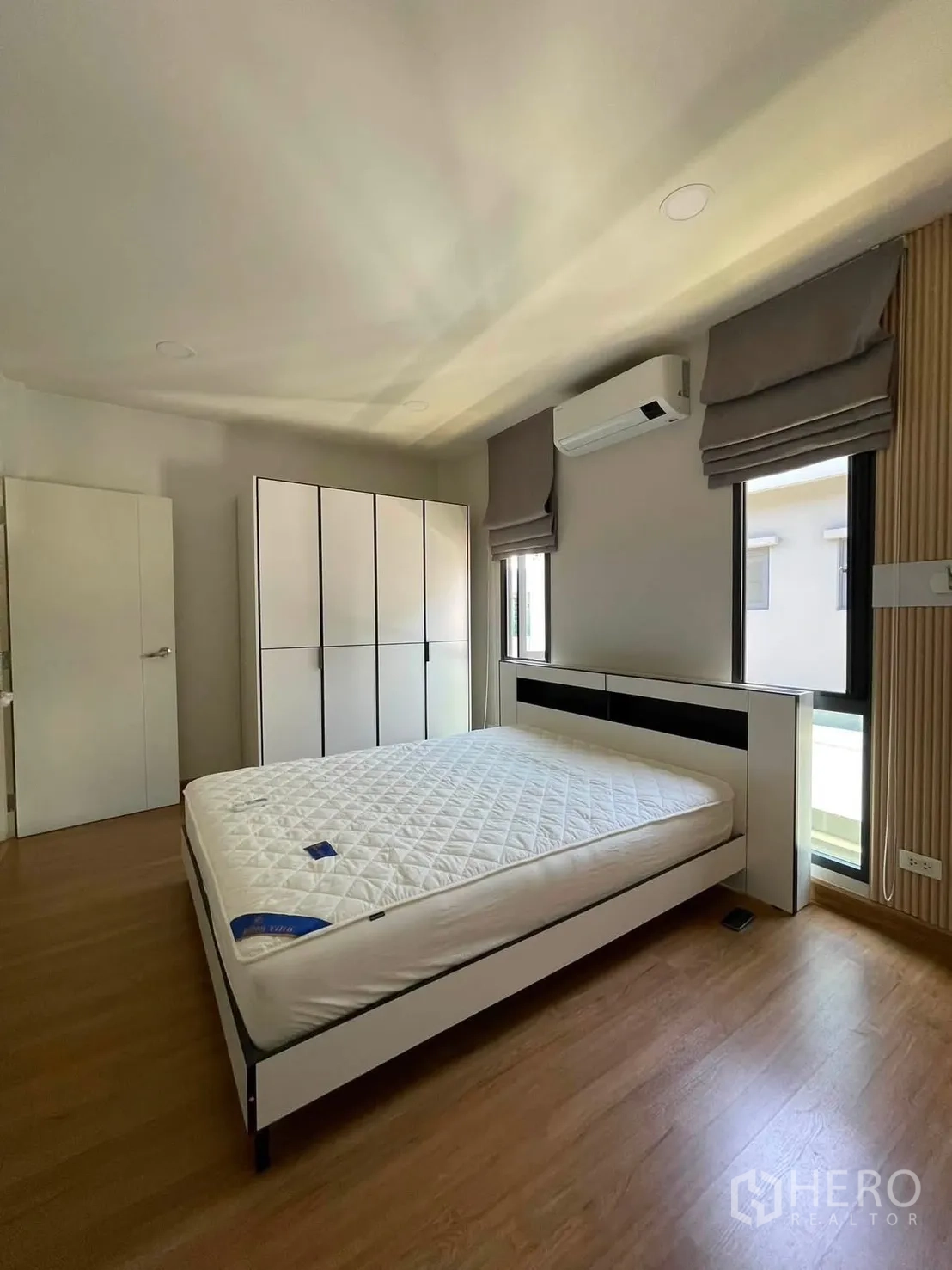 独栋房屋 for rent in Bang Phli, Samut Prakan - 卧室内白色床架、衣柜、空调，两扇带罗马帘的窗与木地板。