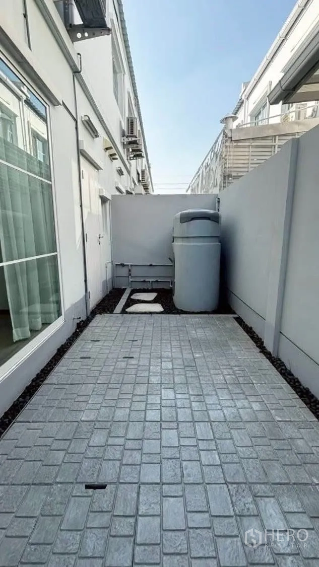 Townhouse for rent in Prawet, Bangkok - Paved backyard utility area with water tank and side service access.