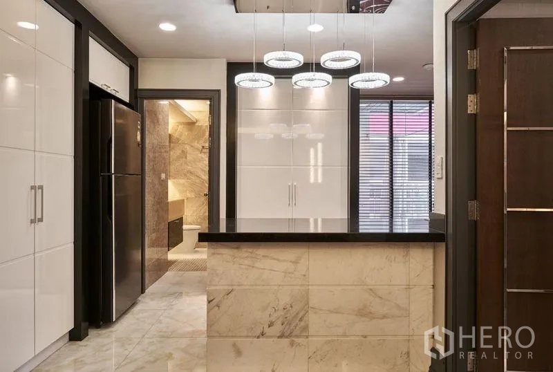 Condominium for sale in Ratchathewi, Bangkok - Kitchen island with marble base, white cabinetry and doorway to bathroom.