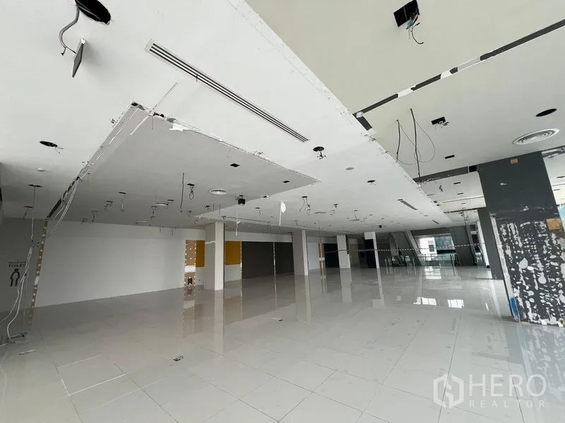 零售空间 出租在Din Daeng, Bangkok - 宽阔零售大厅，裸露灯位，远处可见扶梯，白色反光地砖。