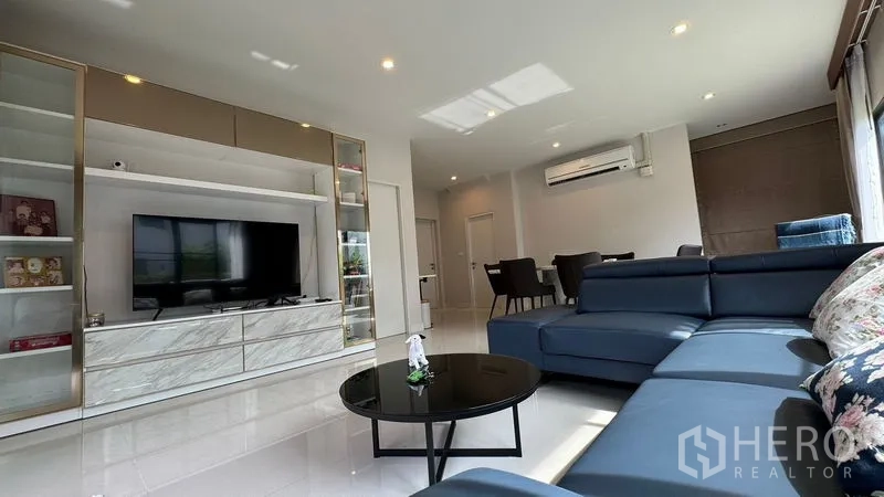 Detached House for rent in Prawet, Bangkok - Living area featuring a TV wall unit with shelving and a sectional sofa.