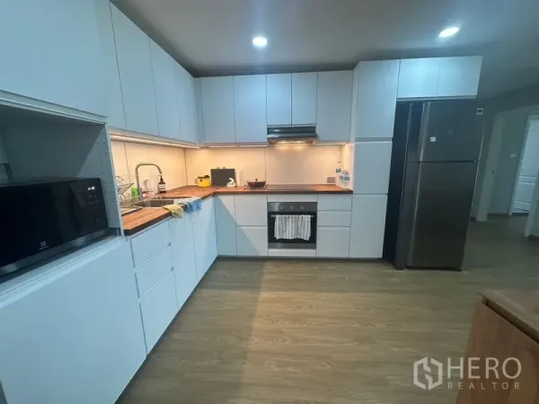 Condominium for rent - Modern L-shaped kitchen with white cabinetry, wood countertops, built-in oven and large fridge.
