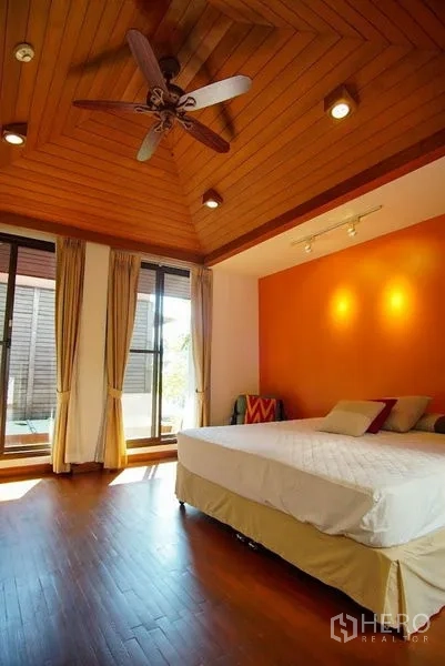 Townhouse for rent in Watthana, Bangkok - Bedroom with warm wood ceiling, ceiling fan, and sliding doors to balcony.