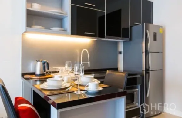 公寓 出租在Khlong Toei, Bangkok - 紧凑厨房，亮黑橱柜、灯带与不锈钢冰箱。