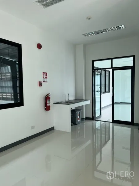 Factory for rent in Bang Sao Thong, Samut Prakan - Office pantry area with sink, fire extinguisher and glass door to warehouse.