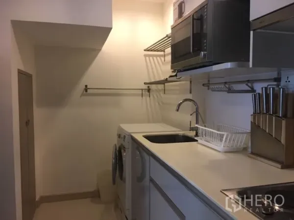 Condominium for rent in Phra Khanong, Bangkok - Compact fitted kitchen with sink, microwave, shelving, and in-unit washer