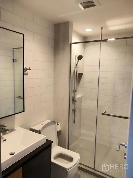Condominium for rent in Chatuchak, Bangkok - Modern bathroom with white subway tiles, glass shower enclosure, and vanity sink.