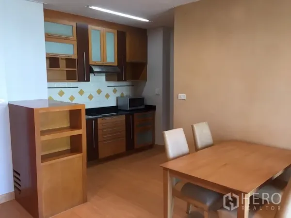 Condominium for rent in Sathon, Bangkok - Compact kitchen with wood cabinets, glass inserts, tiled backsplash and adjacent dining area.