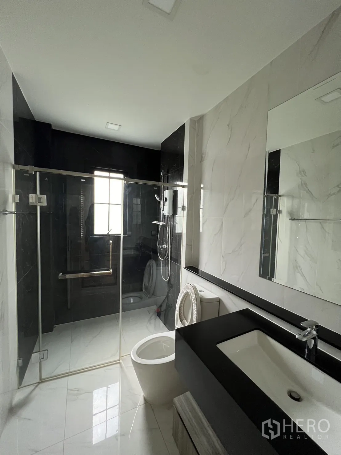 Detached House for rent or sale in Prawet, Bangkok - Contemporary bathroom with glass shower, white marble tiles and black vanity.