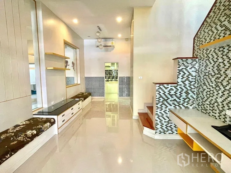 Townhouse for rent in Saphan Sung, Bangkok - Ground‑floor hall with glossy tiles, built‑in seating and mosaic‑tiled staircase with shelving.