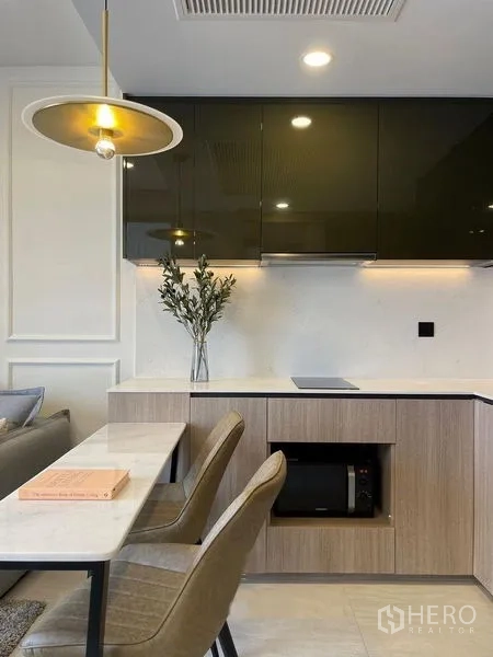 公寓 出租在Pathum Wan, Bangkok - 现代小厨房，亮面吊柜、电磁炉与双人用餐吧台。