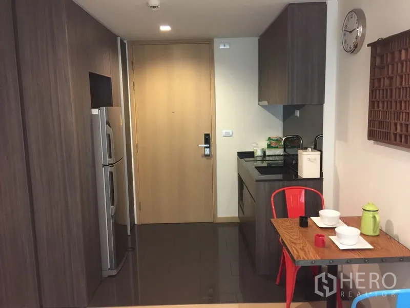 公寓 出租在Watthana, Bangkok - 入户走廊连开放式小厨房，木色大门，双门冰箱与双人餐桌。