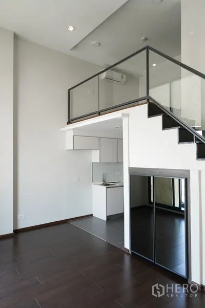 Condominium for sale in Watthana, Bangkok - Double-height living area with a mezzanine level positioned above the compact kitchen.