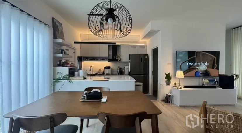 Townhouse for rent in Bang Phli, Samut Prakan - Open‑plan dining and kitchen with island, modern cabinetry, pendant light and TV wall in a bright townhouse.