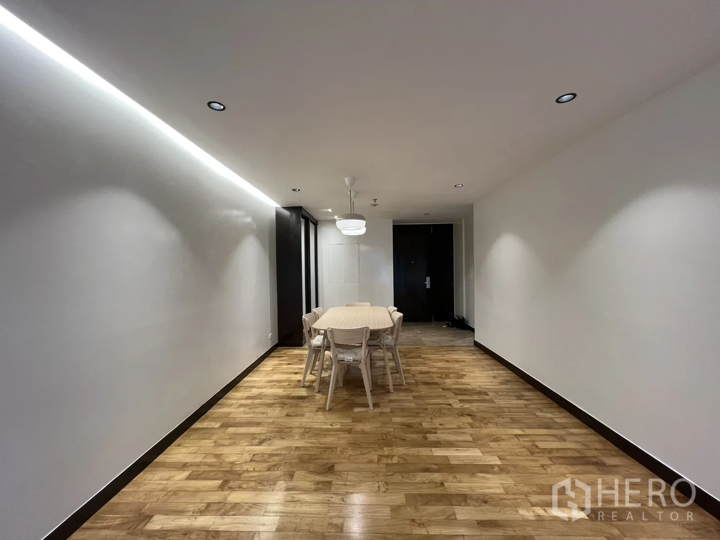 Apartment for rent in Watthana, Bangkok - Wide shot of the dining zone with LED cove lighting, wooden floors, and the main entrance door.
