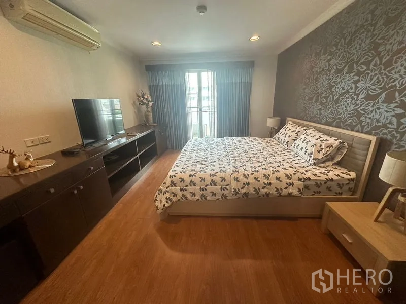 Condominium for rent in Watthana, Bangkok - Primary bedroom with feature wallpaper, king bed, TV cabinet and balcony access.