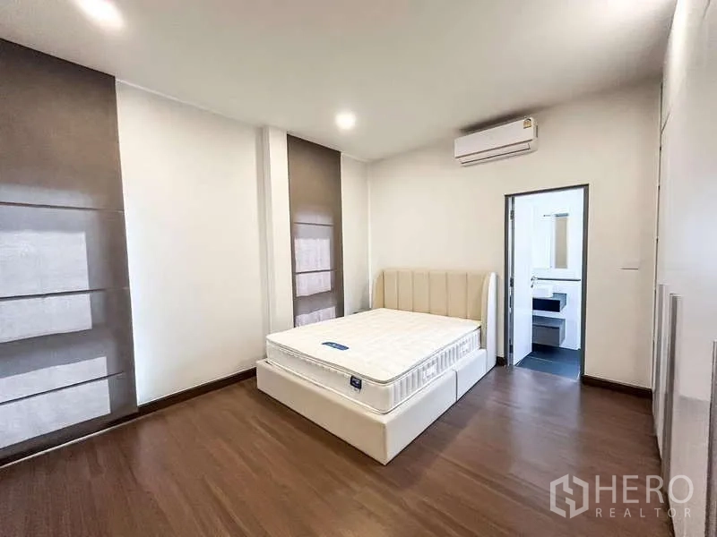 Detached House for rent in Bang Phli, Samut Prakan - Air-conditioned bedroom with neutral decor, wood floor and private bathroom entrance.
