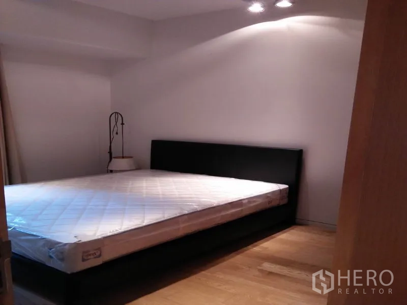 Condominium for rent in Sathon, Bangkok - Bedroom with platform bed, bedside lamp and wood floors under soft lighting.