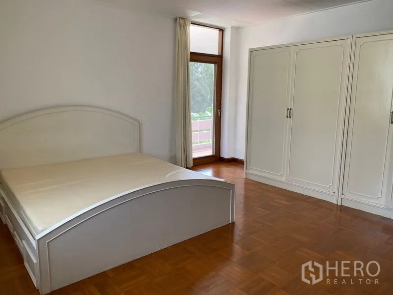 Apartment for rent in Khlong Toei, Bangkok - Master bedroom with built-in wardrobe and door opening to balcony, parquet floor.