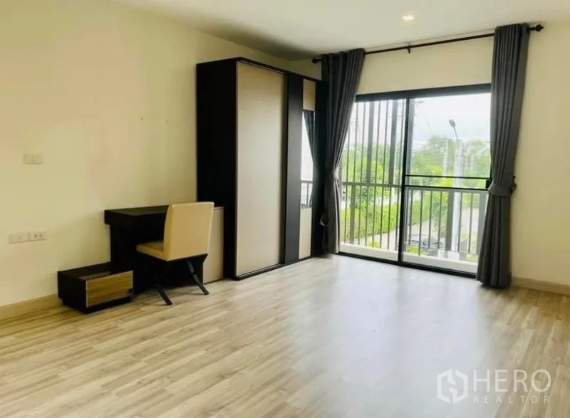 Townhouse for rent in Saphan Sung, Bangkok - Spacious bedroom with desk, wardrobe, sliding doors to balcony and laminate wood flooring.