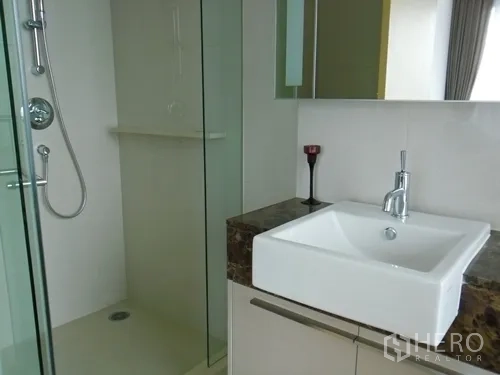 Condominium for rent or sale in Watthana, Bangkok - Bathroom with glass-enclosed shower and square basin on a marble countertop.