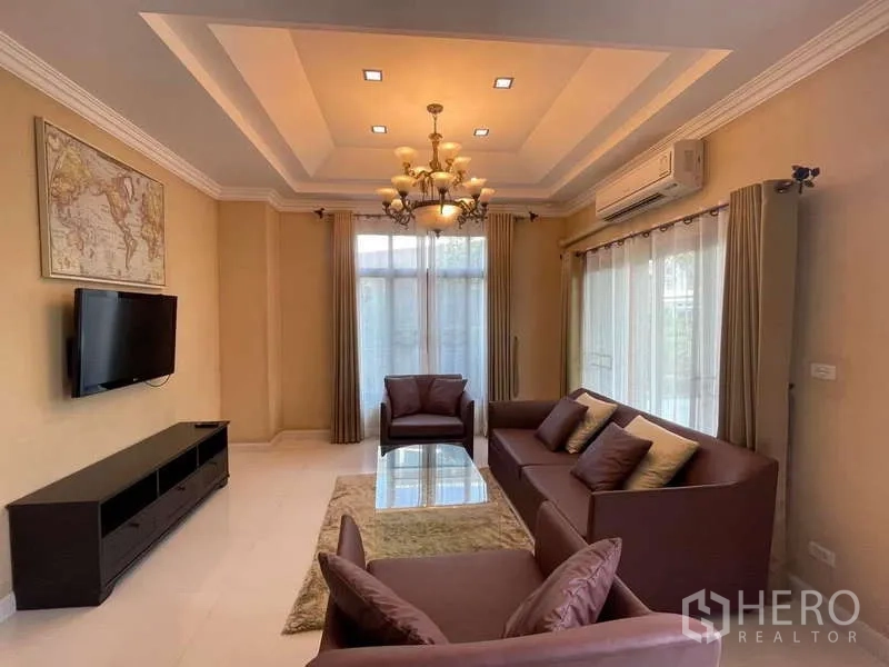独立式住宅 出租在Mueang Nonthaburi, Nonthaburi - 客厅设托盘天花、枝形吊灯、分体空调、沙发与电视柜。