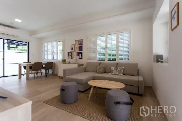 Townhouse for rent in Bang Phli, Samut Prakan - Open-plan lounge and dining area with corner sofa, gallery wall and sliding glass door.