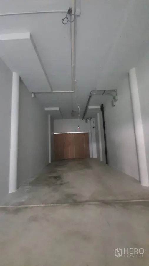 Retail Space for rent in Khlong Toei, Bangkok - Long open‑plan retail unit with concrete floor, high ceiling and exposed conduits facing a roller shutter.