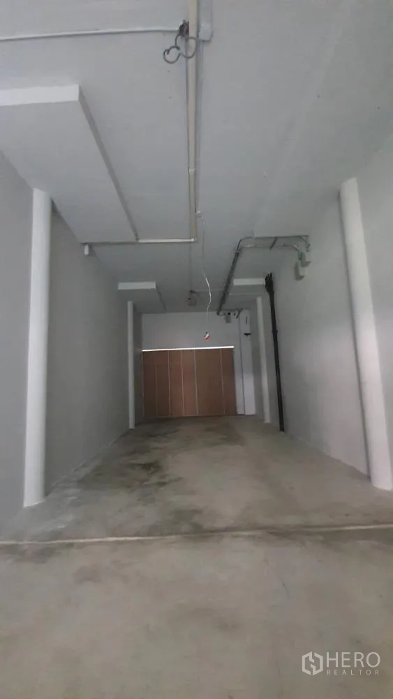 Retail Space for rent in Khlong Toei, Bangkok - Long open‑plan retail unit with concrete floor, high ceiling and exposed conduits facing a roller shutter.