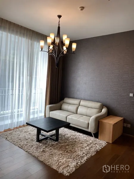 公寓 出租在Watthana, Bangkok - 温馨起居角，米色沙发、长绒地毯、吊灯与通阳台推拉门。