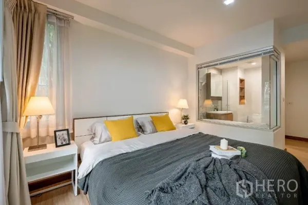 คอนโด ขาย - ห้องนอนใหญ่เตียงคิง พร้อมโคมไฟ และช่องหน้าต่างกระจกมองเห็นห้องน้ำมีอ่างอาบน้ำ