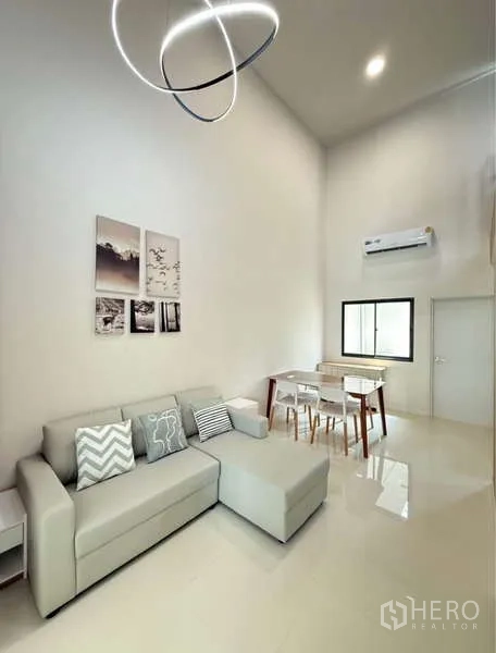 联排别墅 出租在Bang Phli, Samut Prakan - 客厅配转角沙发、现代吊灯与餐桌椅。