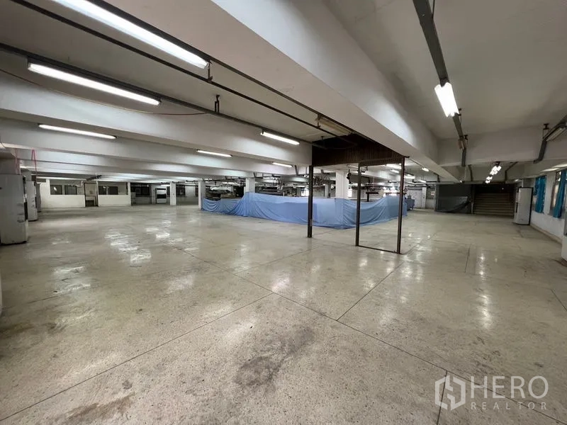 Warehouse for rent in Bang Kapi, Bangkok - Expansive warehouse level with fluorescent lights, support columns and temporary blue partition sheets.