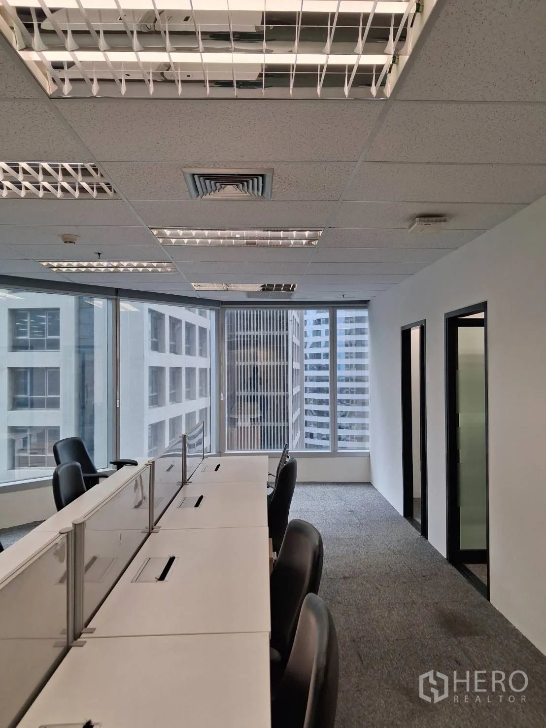 Office Space for rent in Sathon, Bangkok - Open-plan office with bench desks, swivel chairs, carpet flooring and floor-to-ceiling windows with city views.