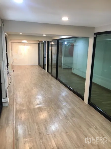 零售空间 出租在Watthana, Bangkok - 狭长展厅走道，一侧为落地玻璃墙与浅色木地板。