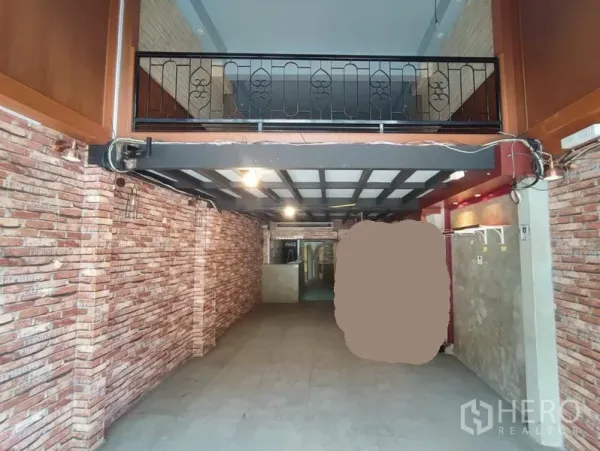 Shophouse for rent in Khlong Toei, Bangkok - Ground-floor retail space with exposed brick walls and a mezzanine with metal railing.