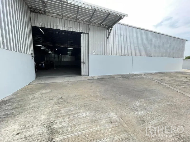 Warehouse for rent in Nakhon Pathom - Corrugated metal warehouse exterior with wide sliding door and a large concrete loading yard in Nakhon Pathom.