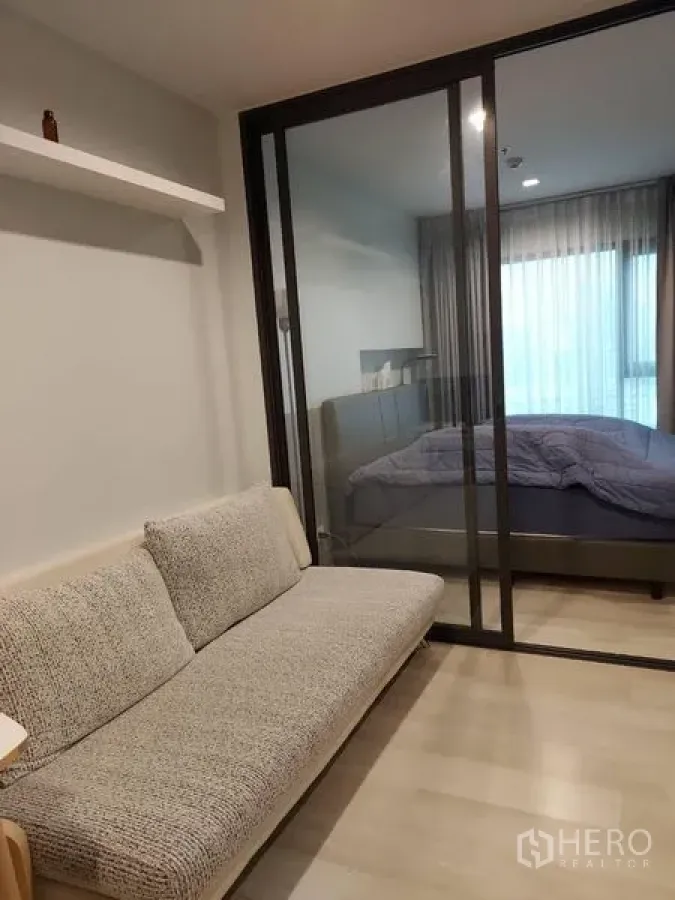 公寓 出售 - 客厅配灰色沙发与玻璃推拉门，相连采光充足的卧室，落地窗帘通透。