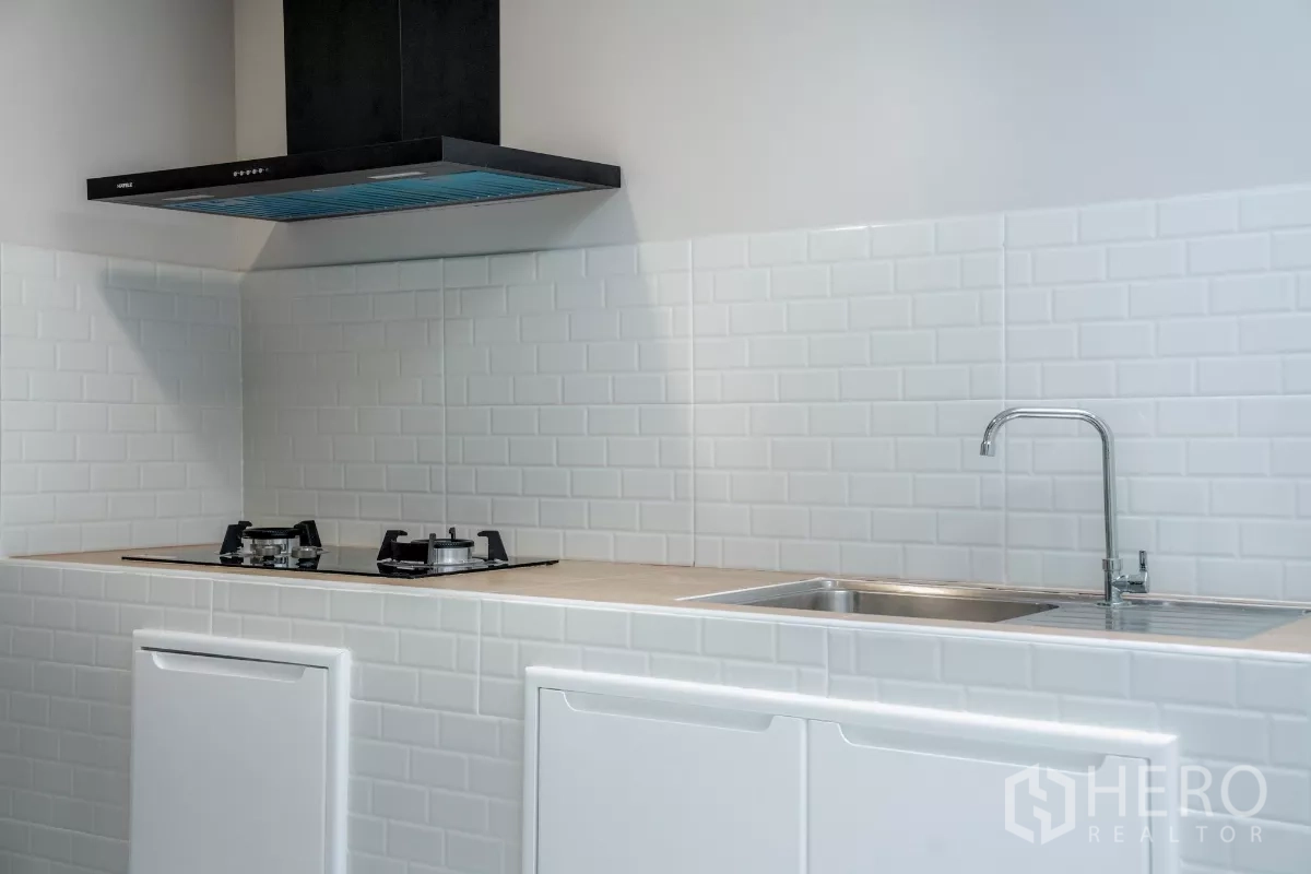 ทาวน์เฮาส์ ขายในWatthana, Bangkok - ครัวสไตล์มินิมอล เตาแก๊ส เครื่องดูดควัน อ่างล้างจานสแตนเลส และผนังกระเบื้องซับเวย์สีขาว