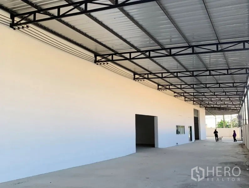 Warehouse for rent in Samut Prakan - Expansive covered drive-through area with metal roof structure alongside the warehouse.