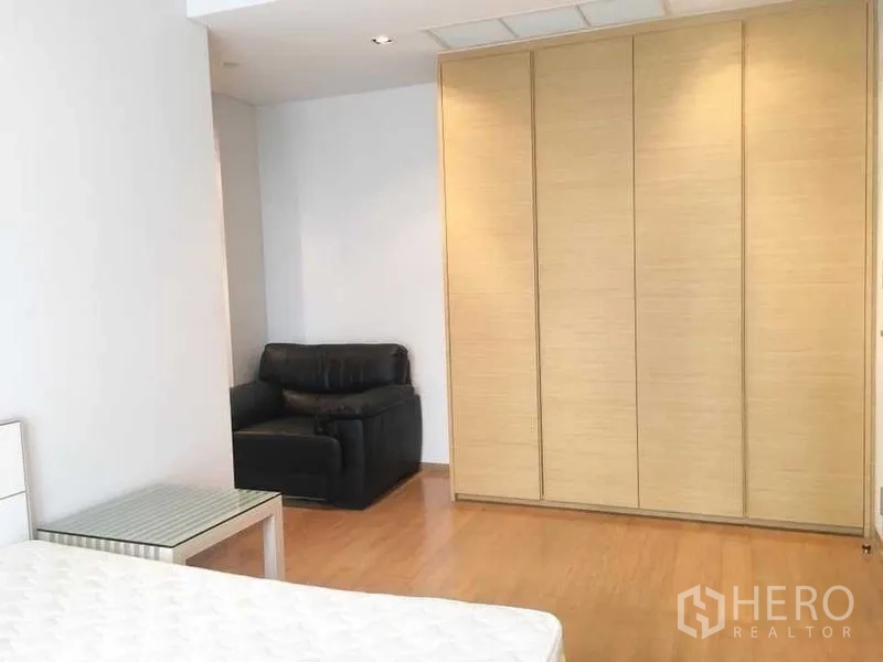 Condominium for rent in Bang Rak, Bangkok - Spacious bedroom featuring a large built-in wardrobe and a black armchair.