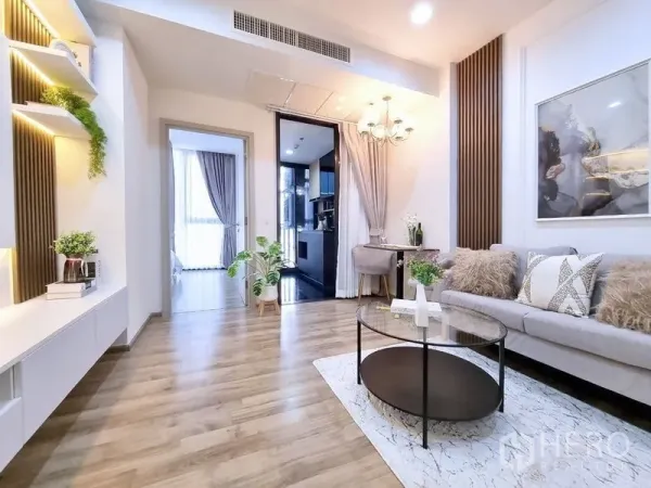 คอนโด ขาย - ห้องนั่งเล่นสว่าง พื้นไม้ ผนังทีวีบิลท์อิน โซฟา และมุมมองไปยังห้องนอนและครัว