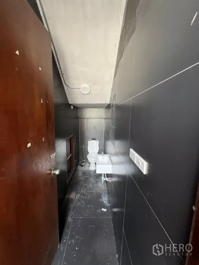 零售空间 出租在Khlong Toei, Bangkok - 狭窄的黑砖卫生间，配马桶和小型洗手盆。