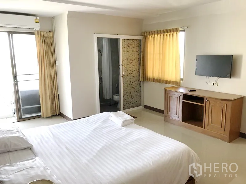 Apartment for rent in Suan Luang, Bangkok - Bedroom with balcony access and ensuite bathroom behind glass door, plus TV cabinet and windows.