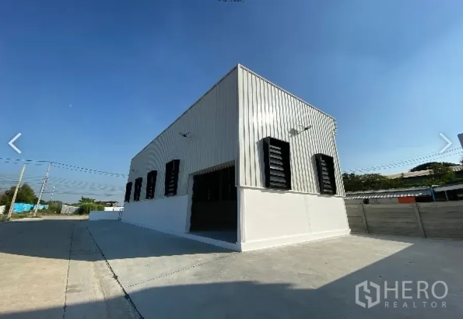 Warehouse for sale in Sai Noi, Nonthaburi - Modern metal-clad warehouse exterior with wide concrete driveway and roller door under a clear blue sky in Sai Noi, Nonthaburi.