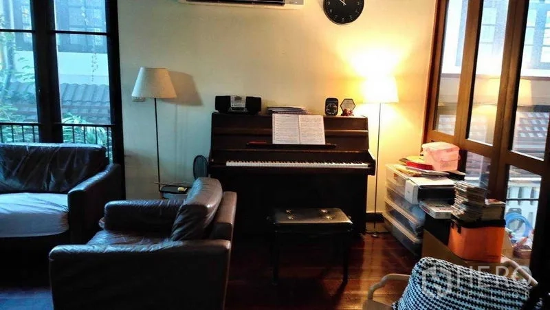 Detached House for sale in Suan Luang, Bangkok - Cozy living room with upright piano, leather sofas, warm lighting and wood flooring beside tall windows.